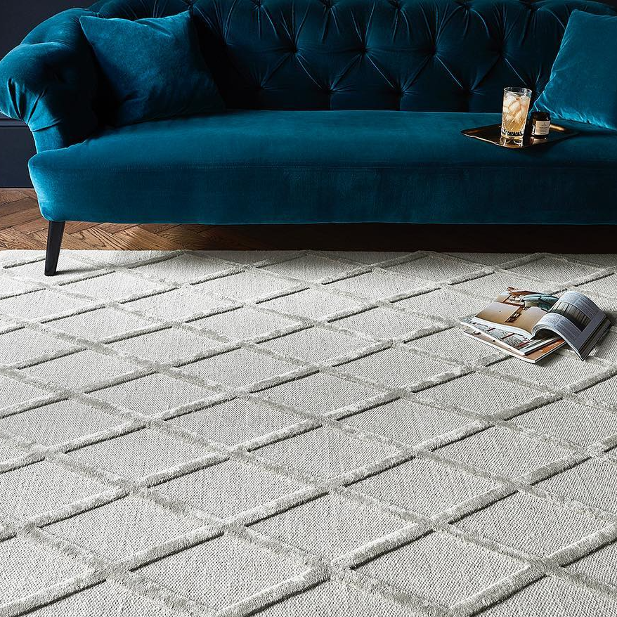 Blue velvet sofa with a coffee table and drinks on a patterned rug in a room.