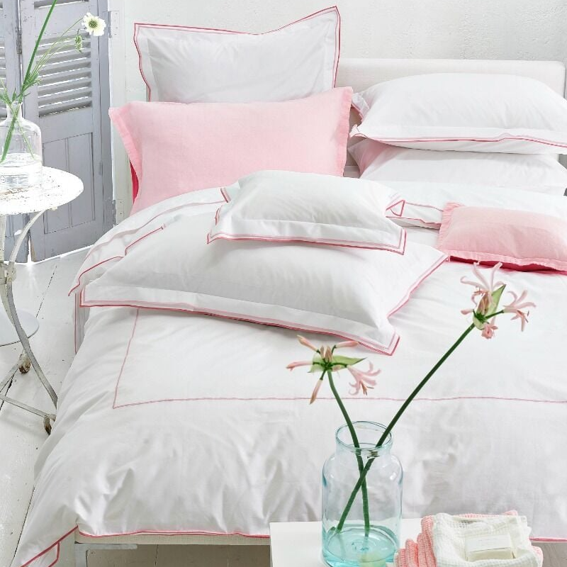 White and pink bedding set on a bed with a vase of flowers on a nightstand.