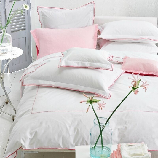 White and pink bedding set on a bed with a vase of flowers on a nightstand.