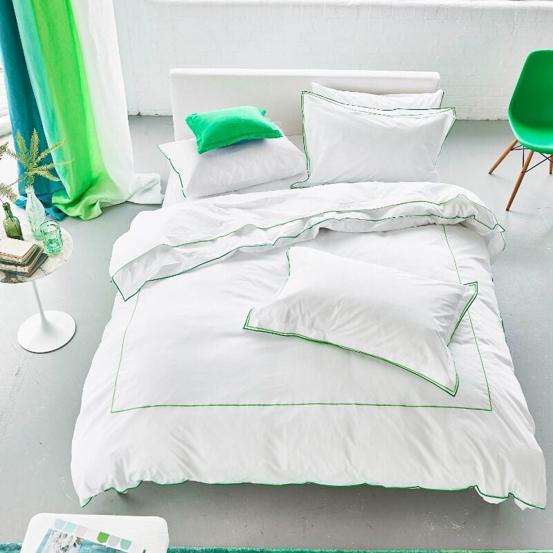 White bedding set with green accents on a bed in a bright room with green curtains.