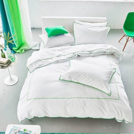White bedding set with green accents on a bed in a bright room with green curtains.
