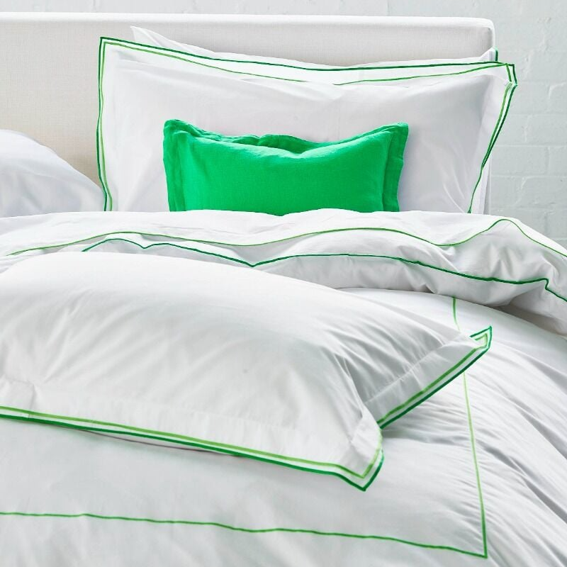 White bedding set with green trim on a bed in a bright room.