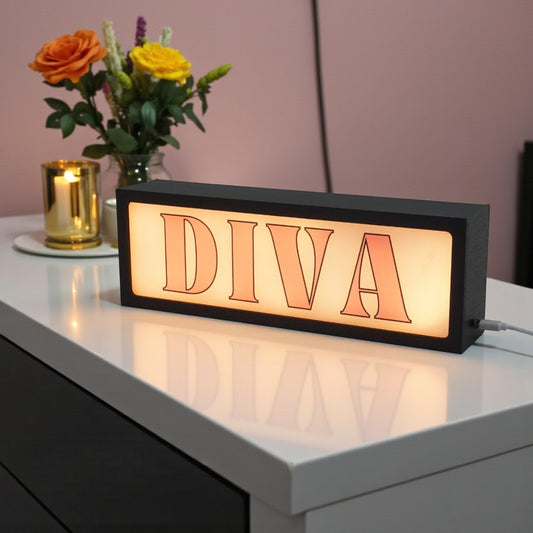Decorative light box with 'DIVA' text on a table with flowers and a candle.