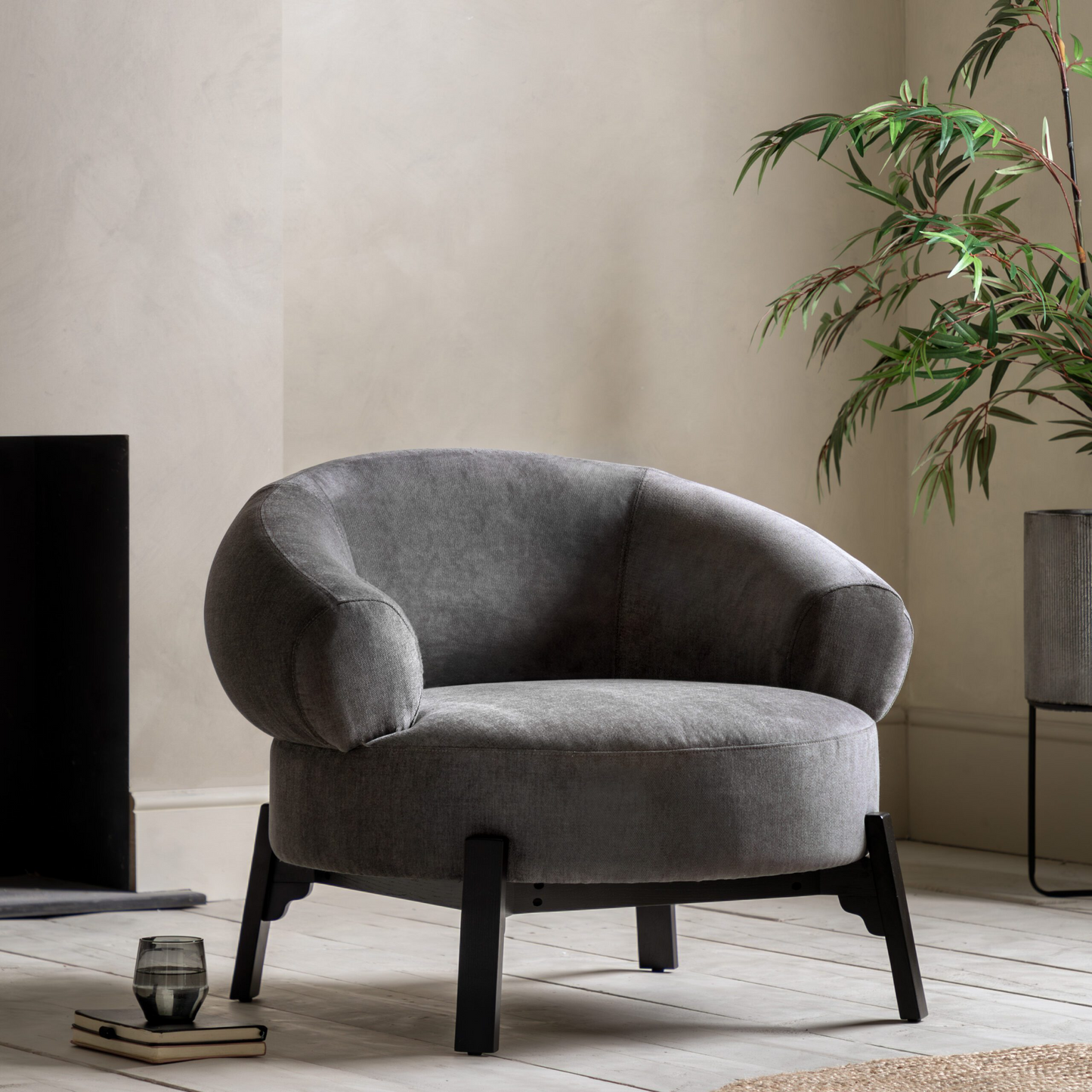 Gray armchair in a room with a plant and books on a wooden floor.