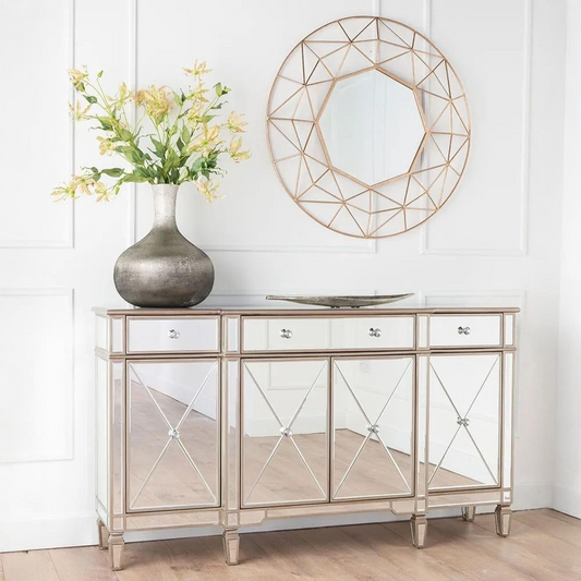 Decorative mirror with geometric design above a mirrored console table with floral arrangement.