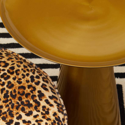Round ottoman with leopard print pattern next to a round mustard-colored table on a black and white striped rug.
