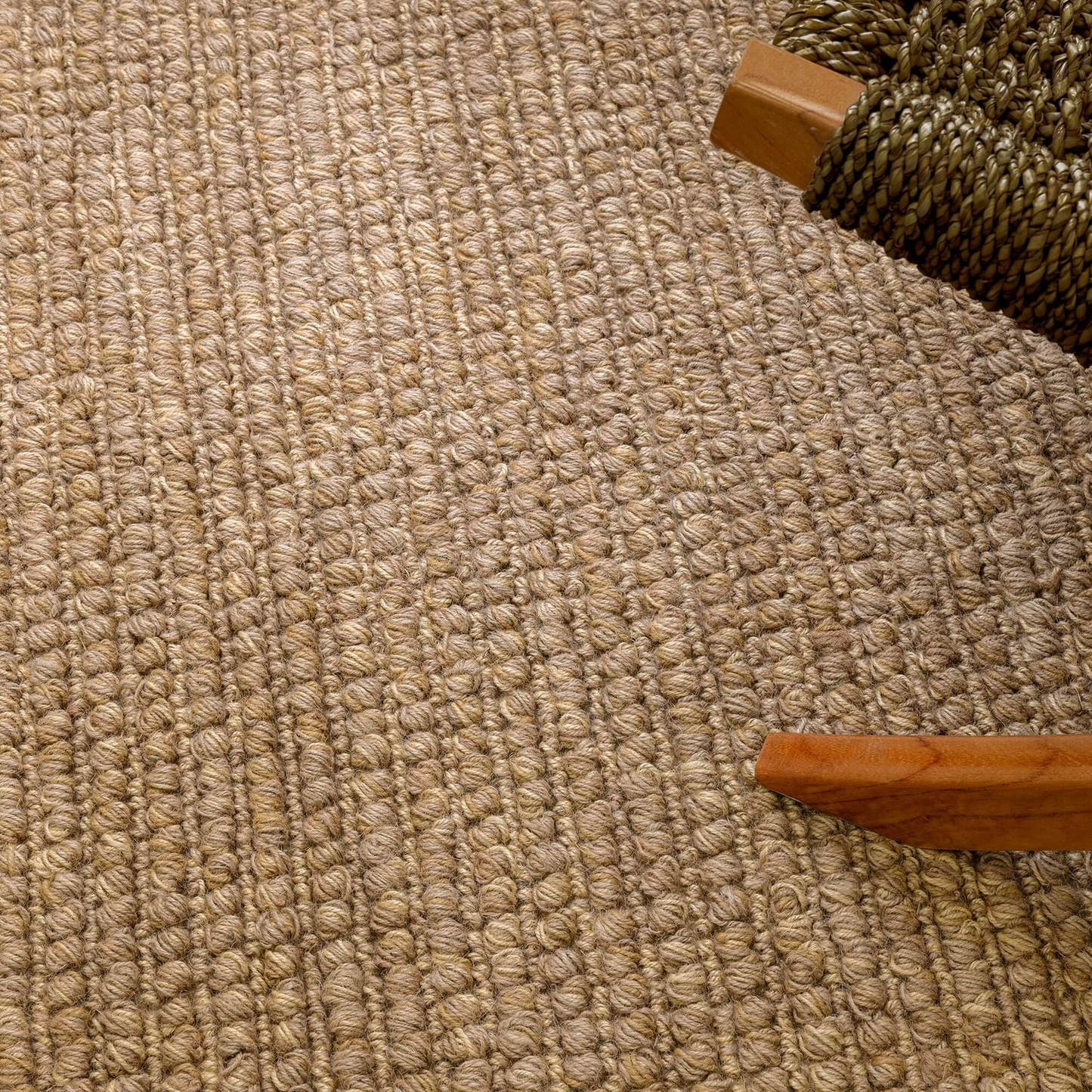 Close-up of a textured beige carpet with wooden furniture legs visible.