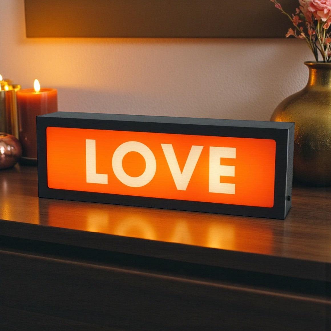 Rectangular LED sign with 'LOVE' on an orange background, placed on a wooden surface.