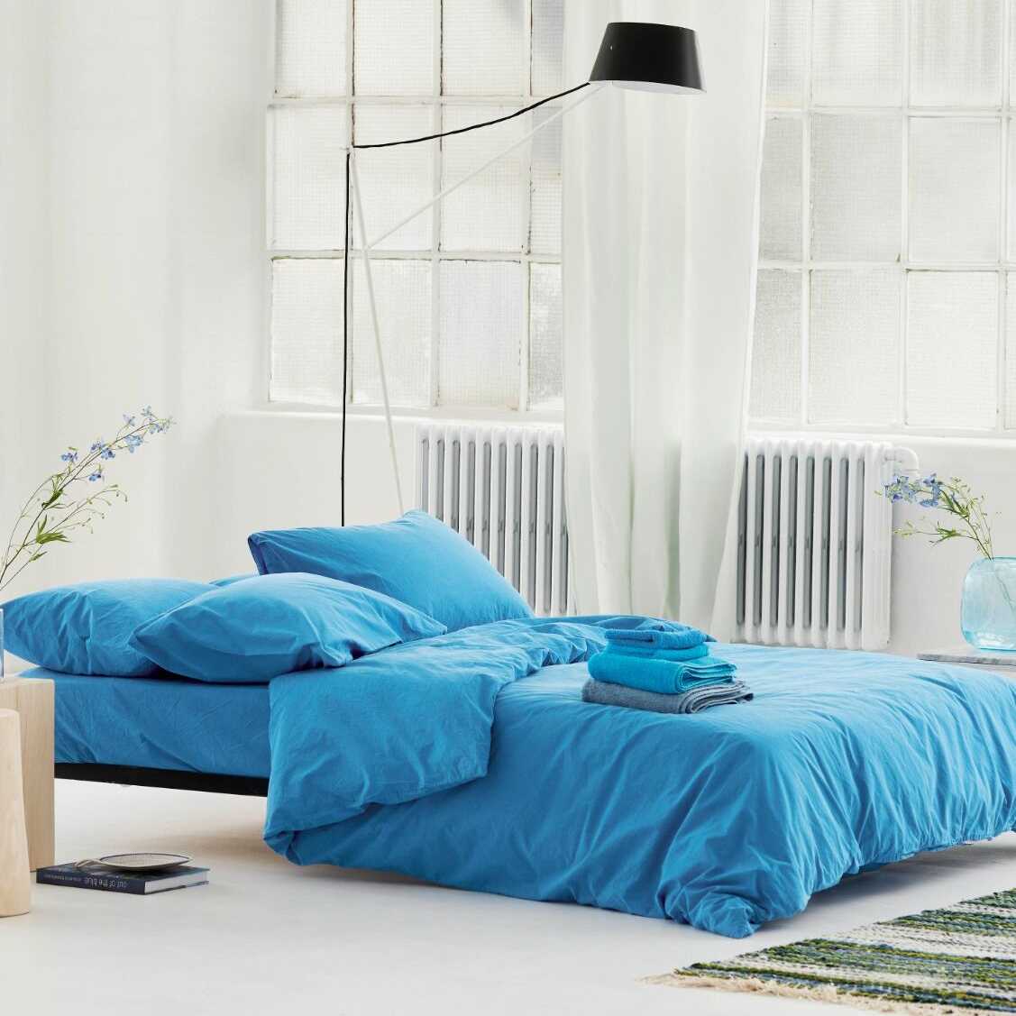 Blue bedding set on a bed in a bright room with large windows.