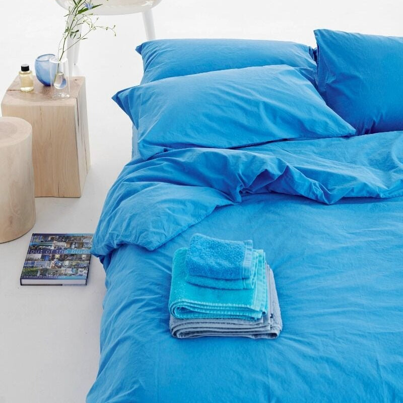 Blue bedding set on a bed with a wooden chair and side table in the background.