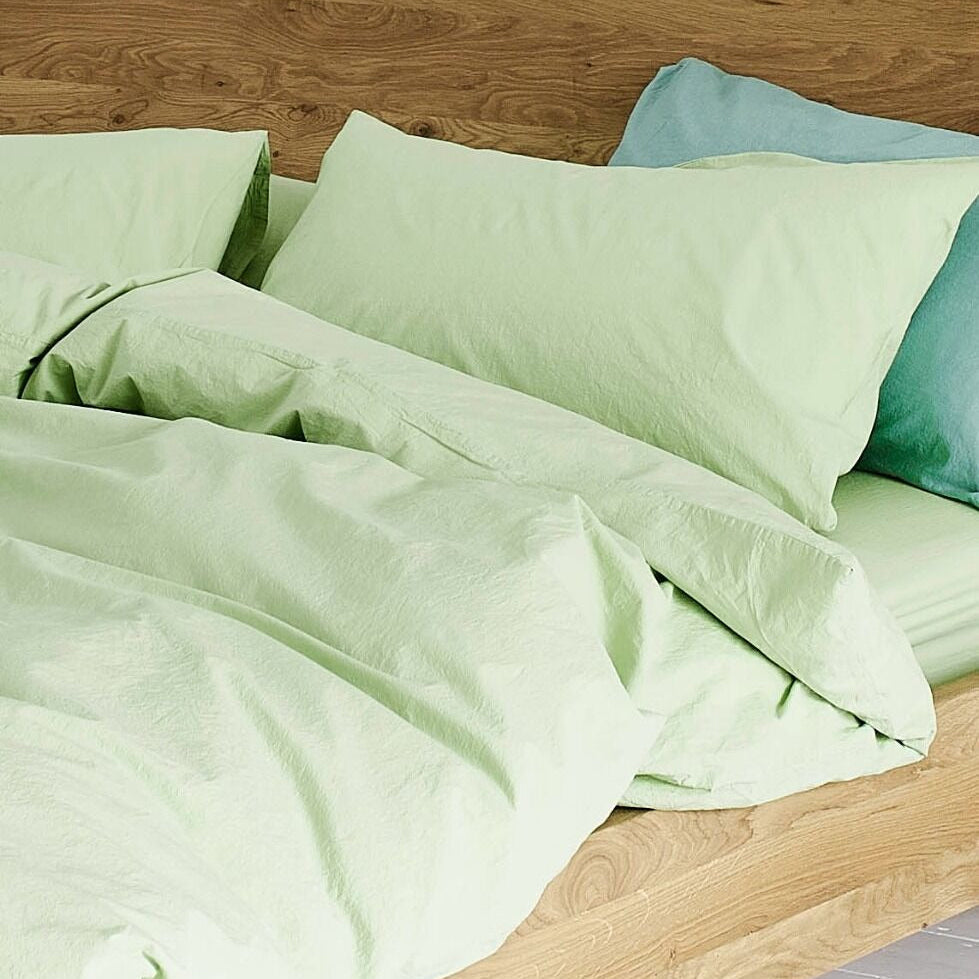 Light green bedding set on a wooden bed frame.