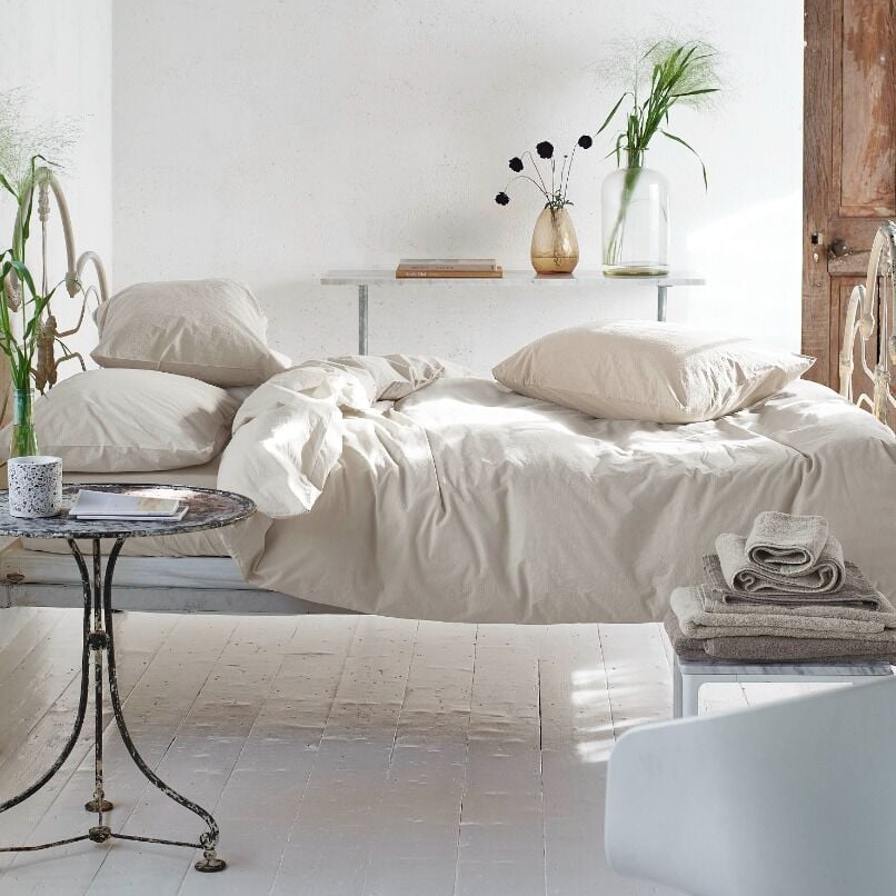 Neatly made bed in a bright bedroom with a chandelier and decorative items.