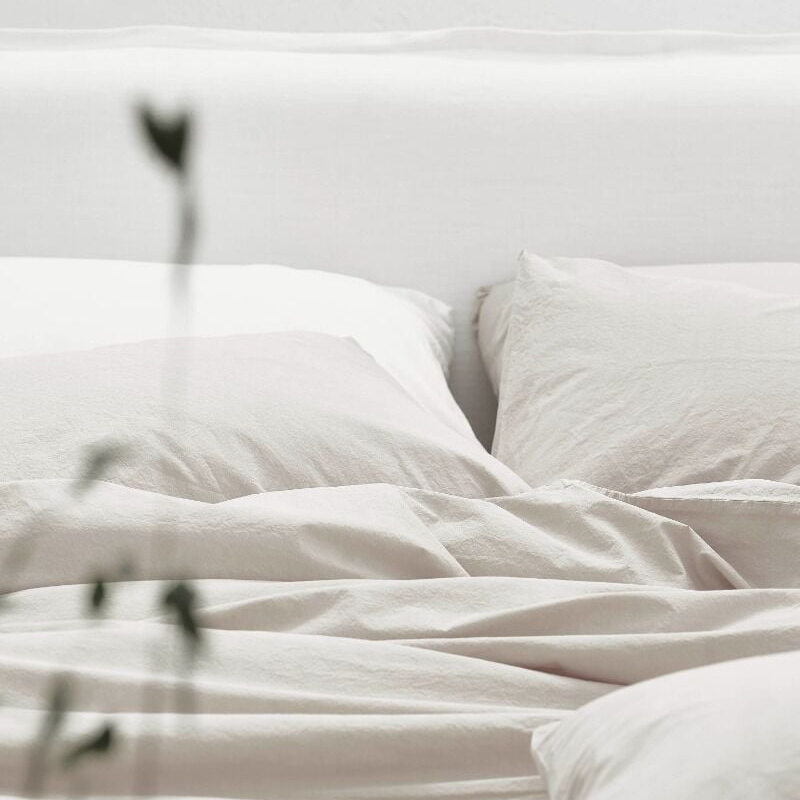 Neatly made bed with white bedding and pillows on a light background