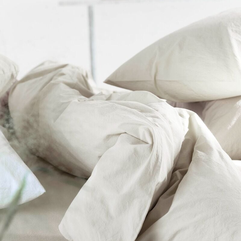 Neatly made bed with beige bedding and pillows in a softly lit room.