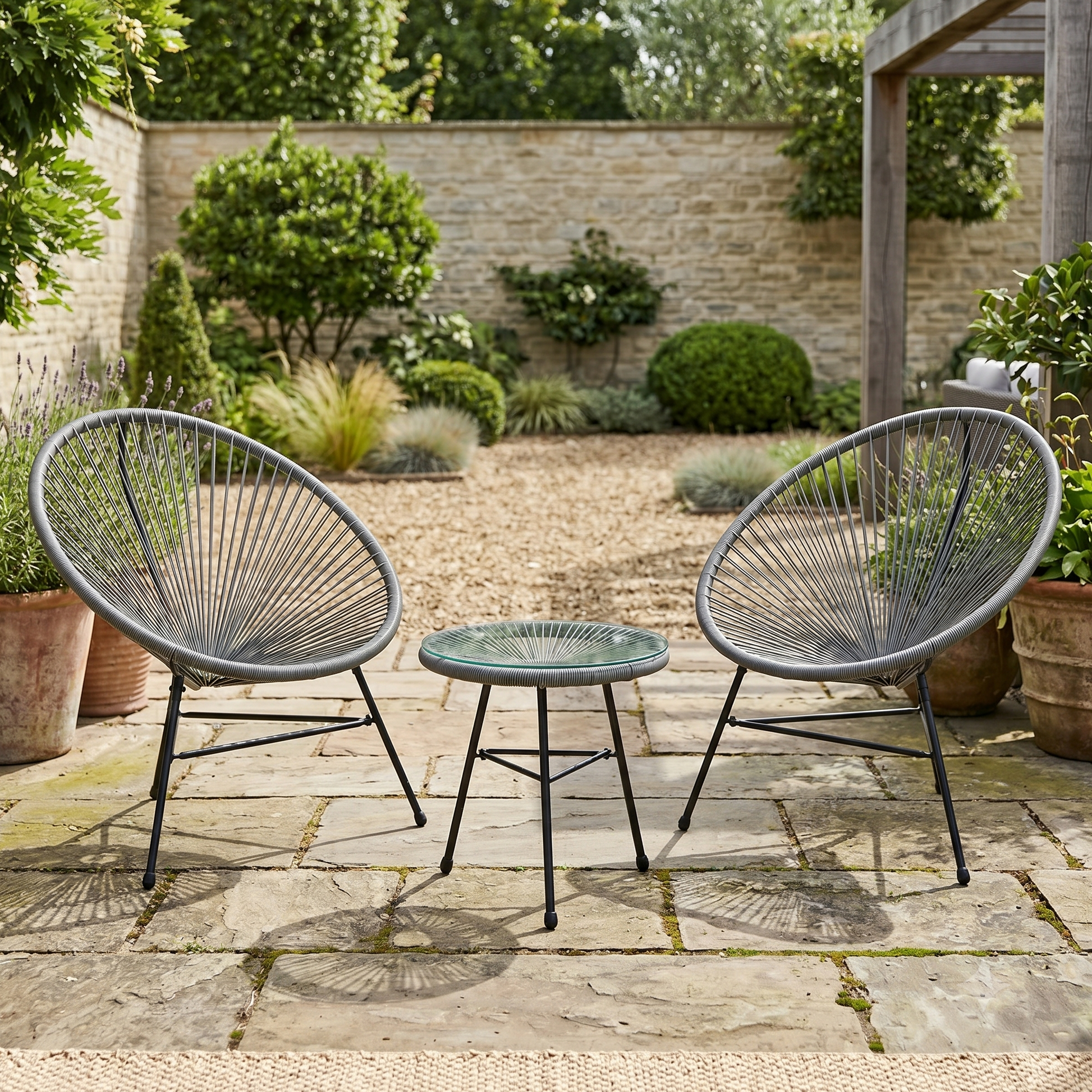 Two gray outdoor chairs with a small table on a stone patio with garden background