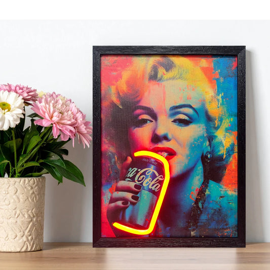 Framed artwork of a colorful depiction of a Marilyn Monroe holding a Coca-Cola bottle, placed on a surface with flowers in the background.