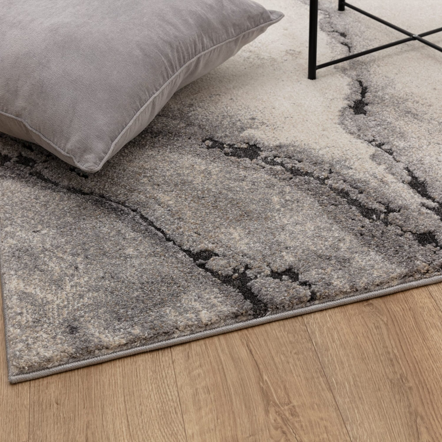 Gray rug on a wooden floor with a pillow and chair corner.