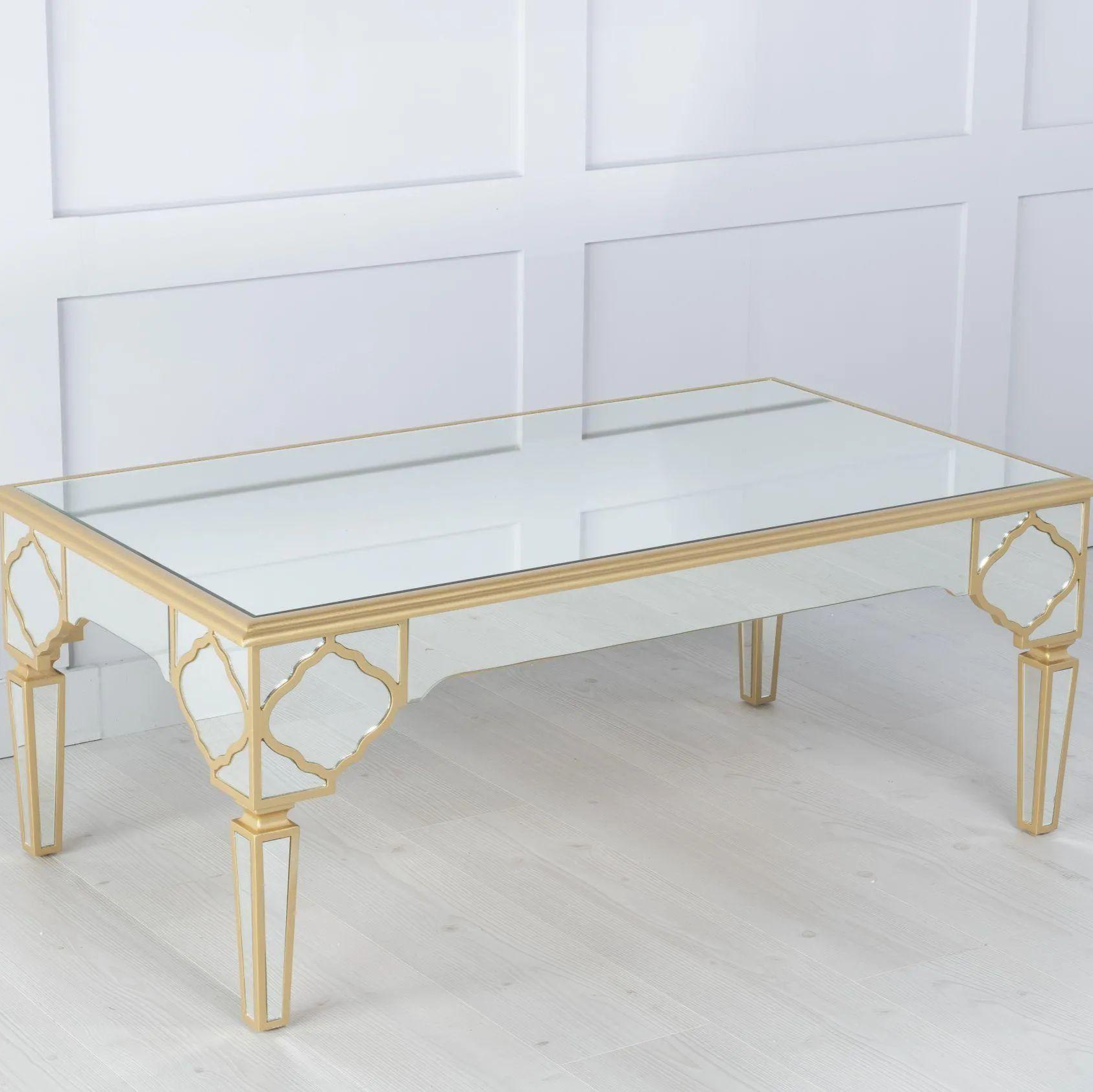 Gold-framed glass coffee table against a white paneled wall.