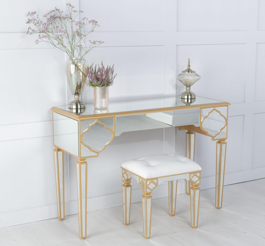 Glass desk with gold frame and white stool against a white wall