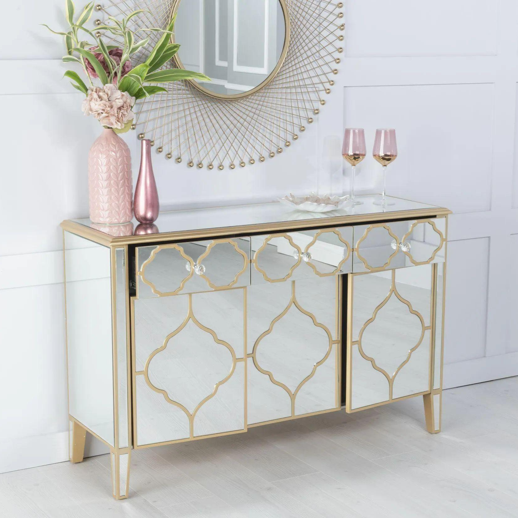 Decorative console table with mirror finish and gold geometric patterns, placed against a white tiled wall.