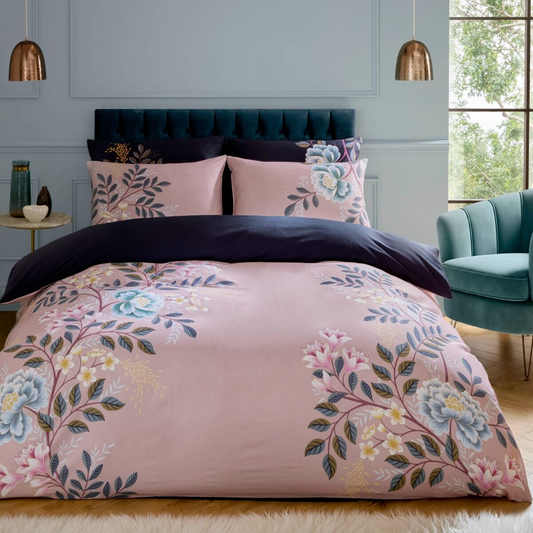 Floral bedding set on a bed in a bedroom with a teal chair and window.