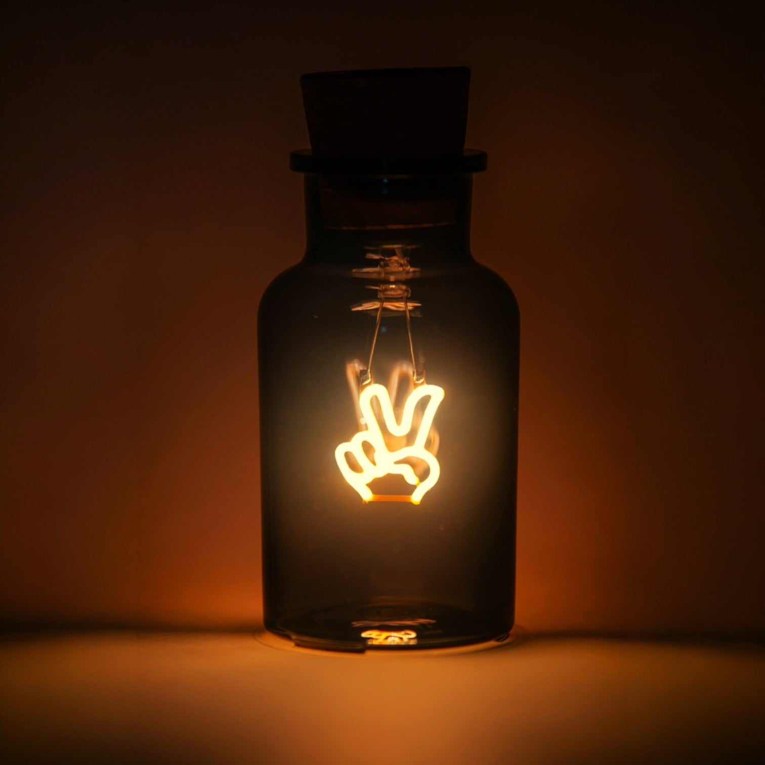 Decorative light bulb shaped like a peace sign inside a dark glass bottle on a dark background