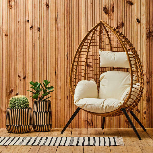 Wicker egg chair with white cushions against a wooden wall.