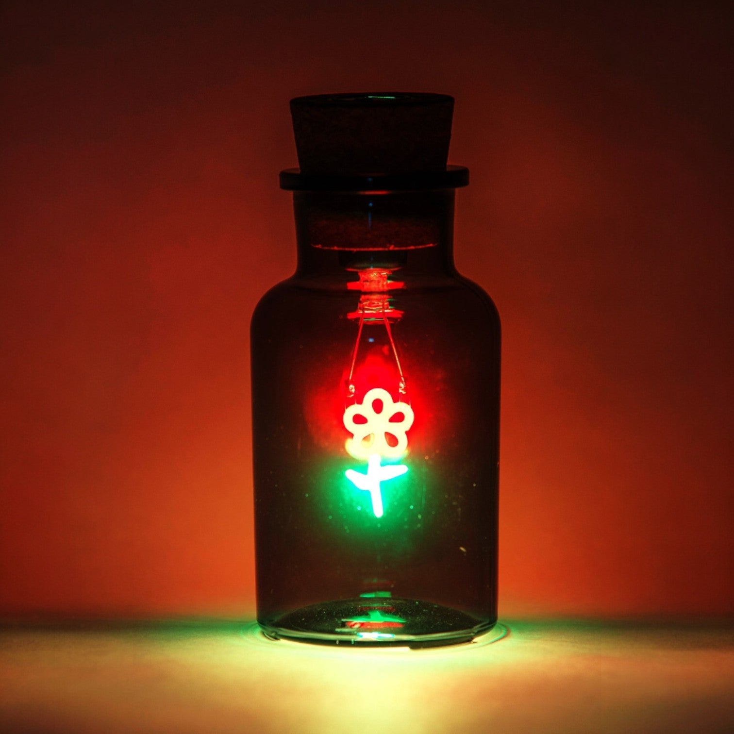 Glass bottle with a floral design light inside against a red background