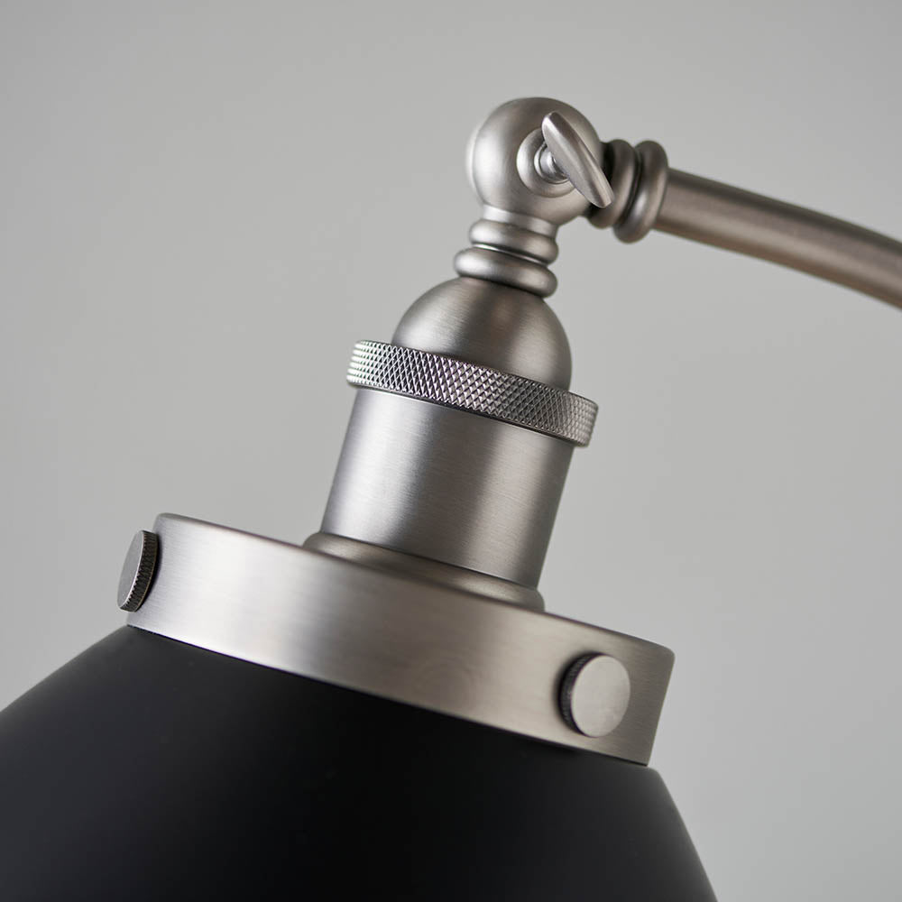 Close-up of a lamp with a metallic arm and black shade on a gray background
