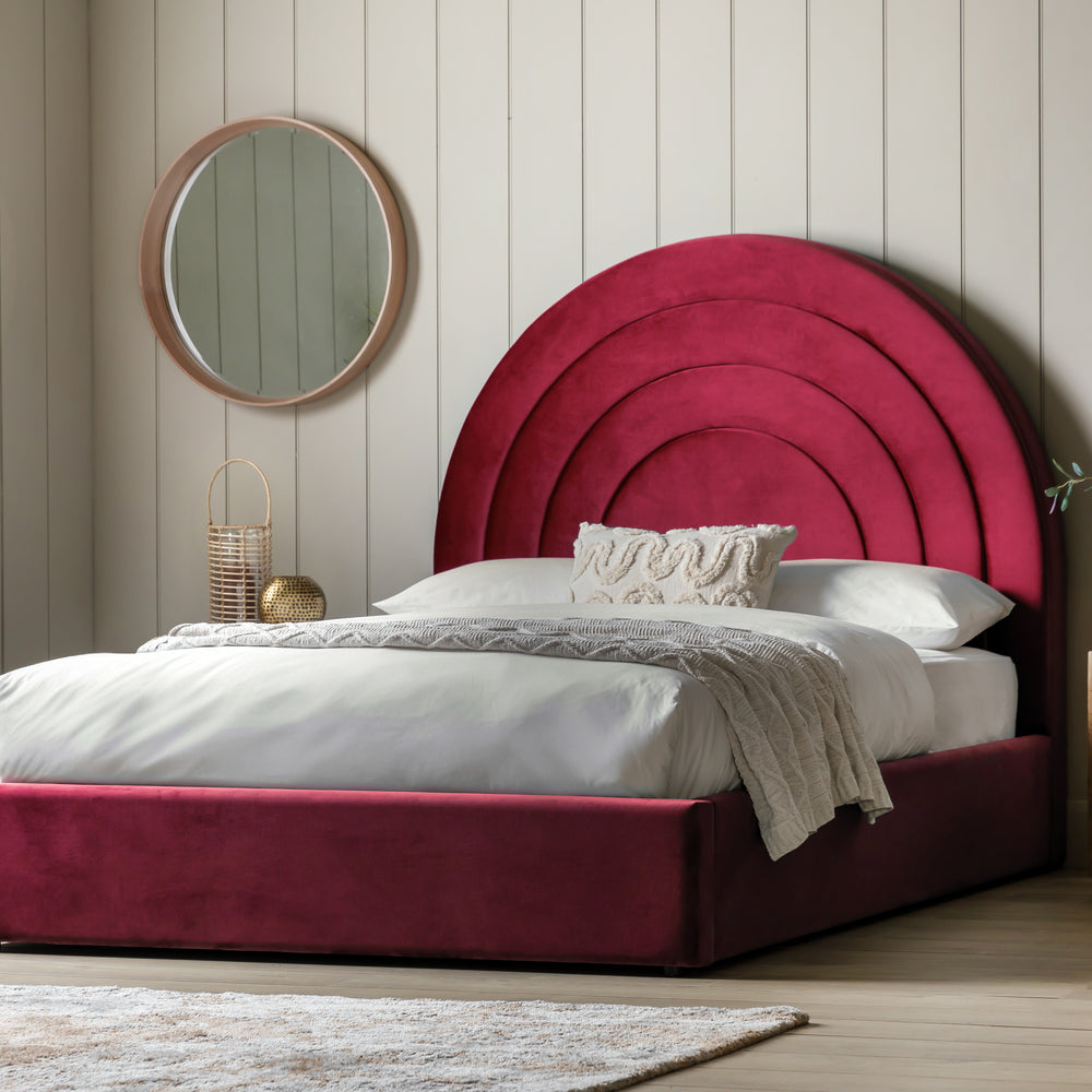Bedroom with a large red headboard and round mirror on the wall.