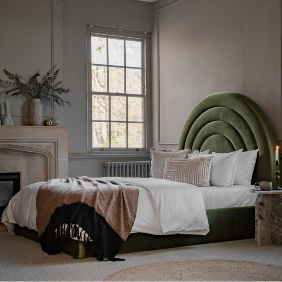 Neatly made bed with a green headboard in a bedroom setting.