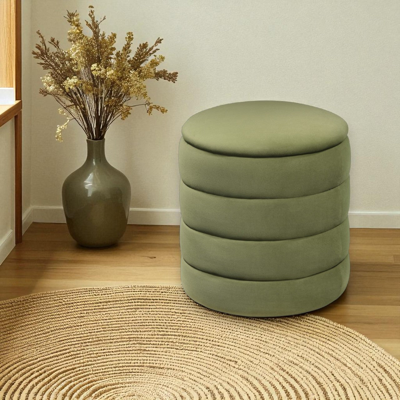 Green ottoman with stacked cylindrical design on a wooden floor next to a vase with dried flowers.