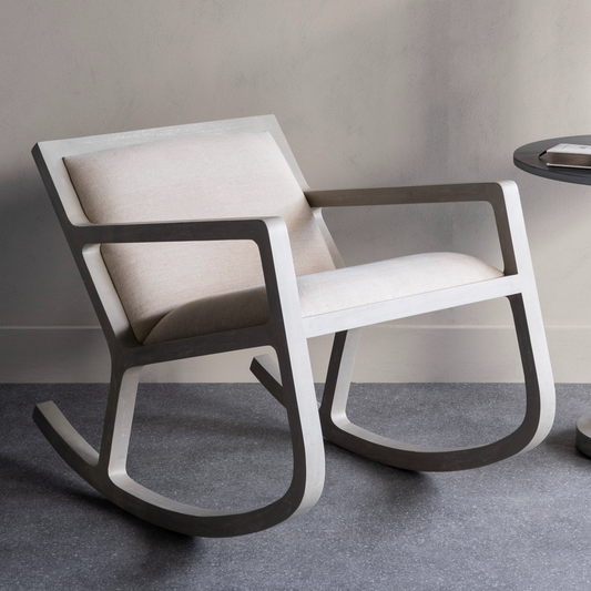 Modern rocking chair with wooden frame and white cushion on a gray floor.