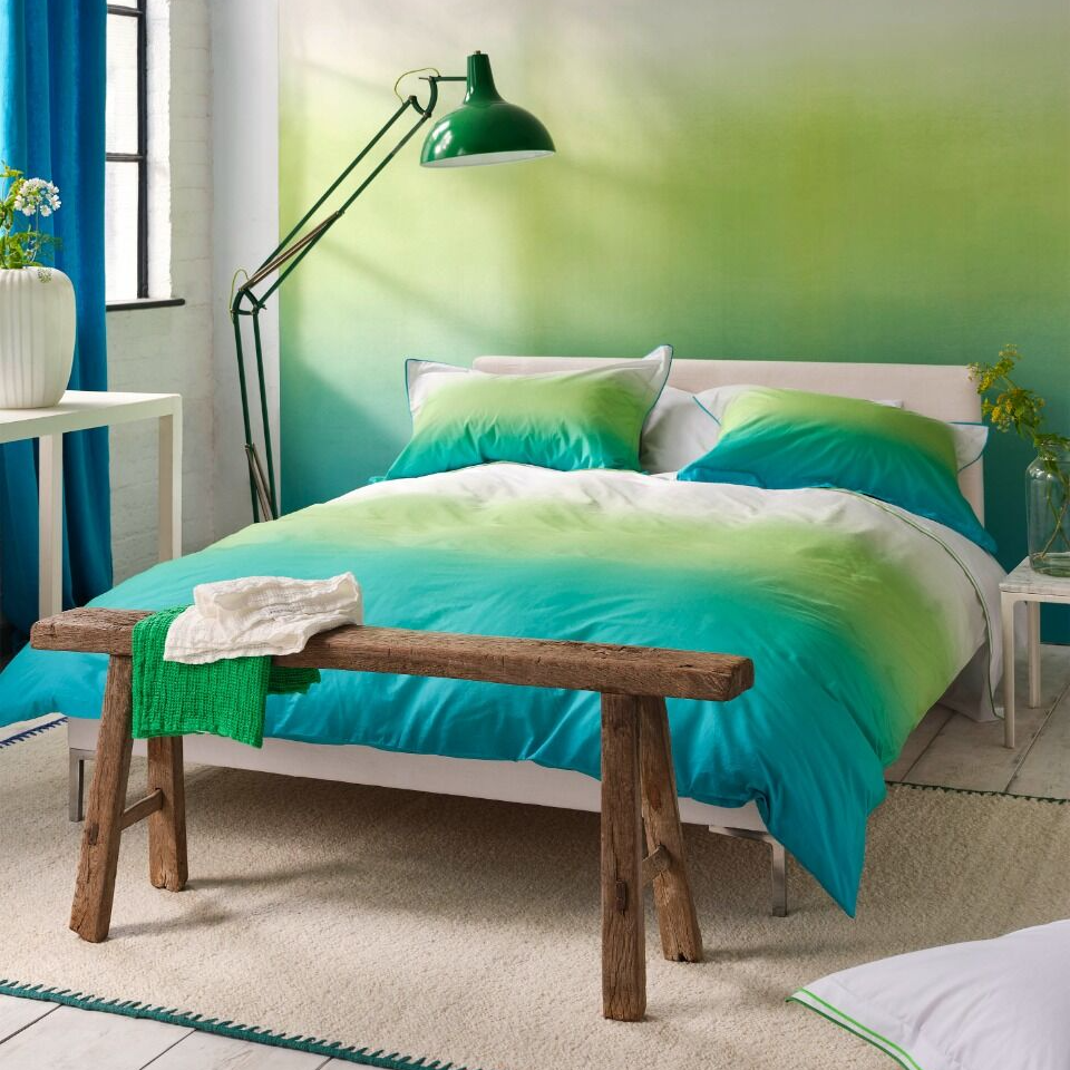 Modern bedroom with green and blue gradient wall, wooden bench, and decorative elements.