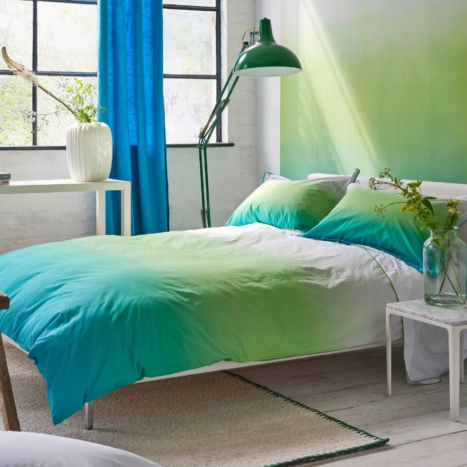 Bedroom with green and blue gradient bedding, white walls, and a lamp.