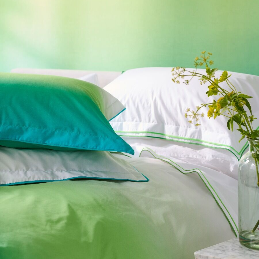 Green and white bedding with a plant on a table in the corner.
