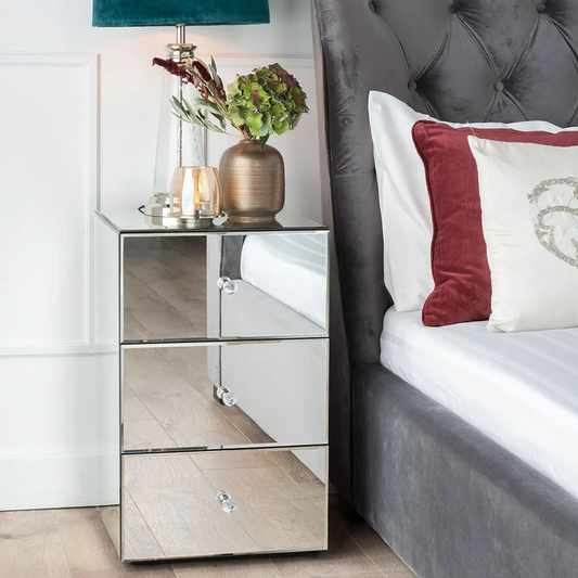 Mirrored nightstand with decorative items next to a bed with pillows.