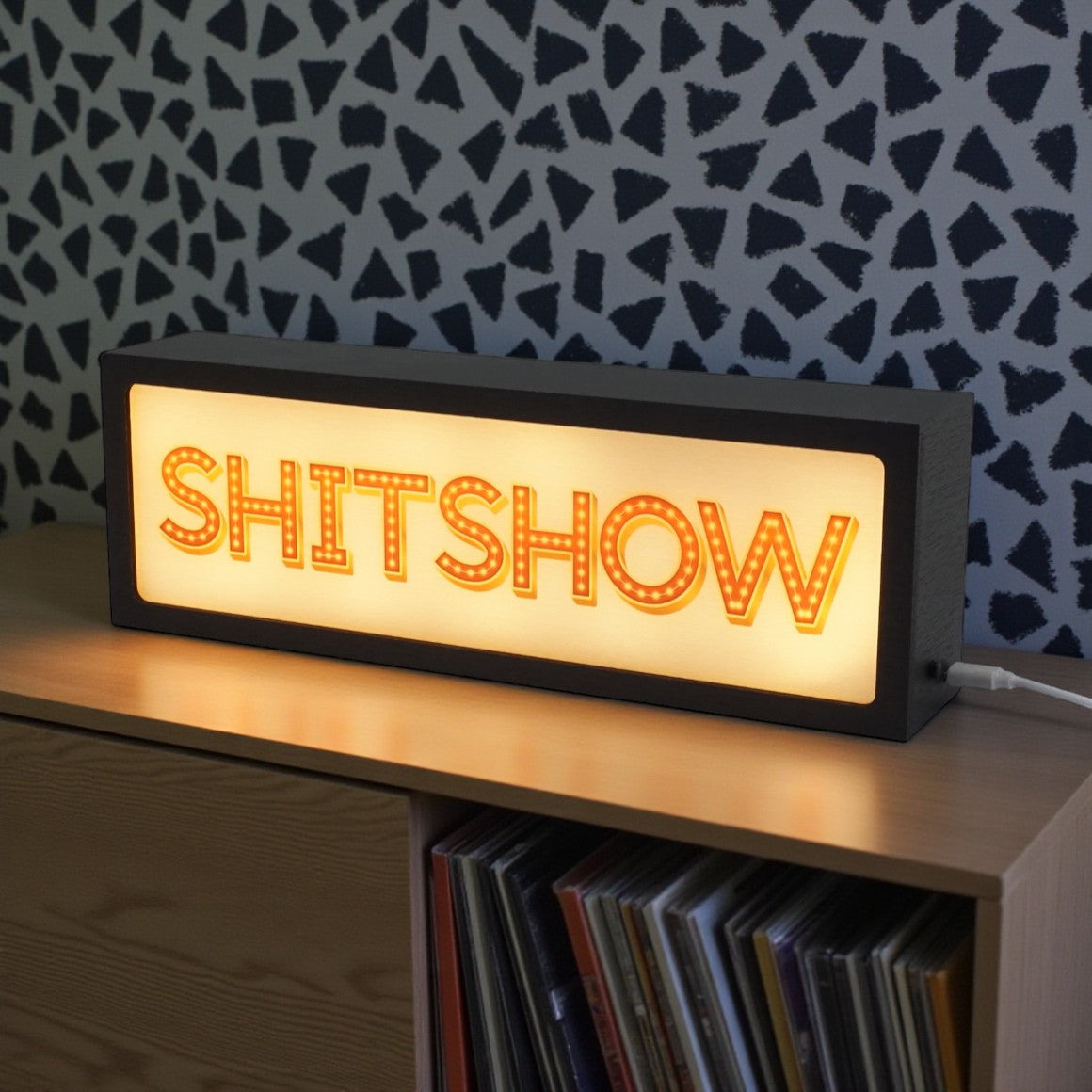Neon sign with 'SHITSHOW' text on a wooden surface with vinyl records in the background.