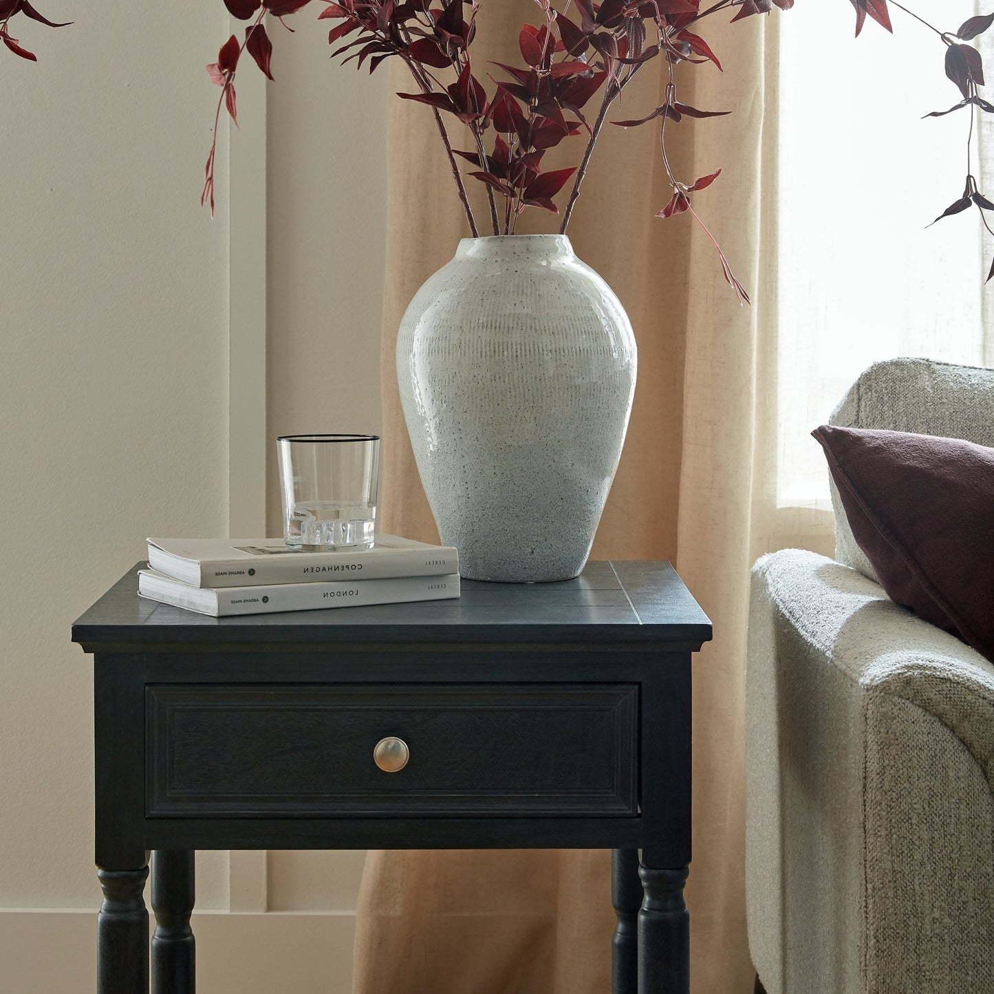 Decorative vase with red leaves on a black side table in a living room setting.