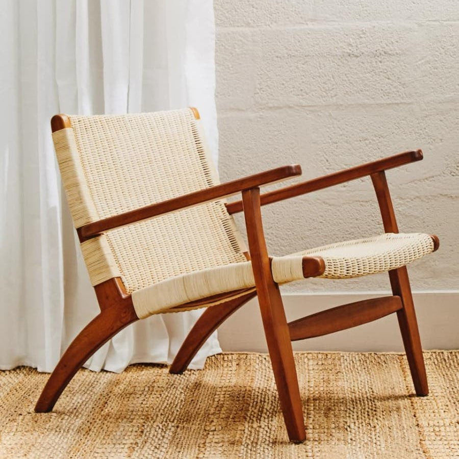 Wooden armchair with woven seat and backrest in a room with white curtains and textured wall.